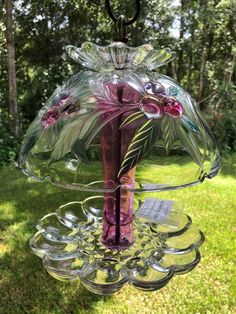 a glass vase with flowers hanging from it's side in the grass next to trees