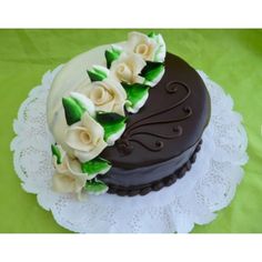 a chocolate cake decorated with white flowers and green leaves on a lace doily in front of a green background