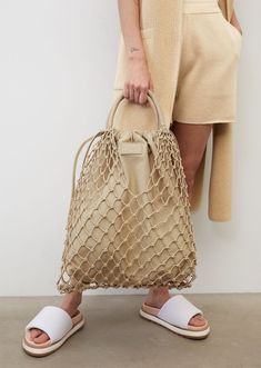 a woman is holding a beige bag in front of her legs and wearing white sandals