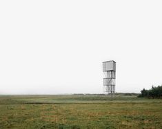 a tall white tower sitting on top of a lush green field next to a forest