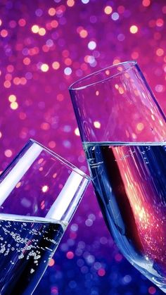 two wine glasses filled with liquid against a purple and pink background that looks like glitter