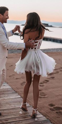 a man in a white suit dancing with a woman on a boardwalk near the ocean