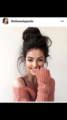 a woman with her hand on her face wearing a pink sweater and smiling at the camera