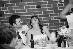 a bride and groom laugh as they sit at a table in front of their guests