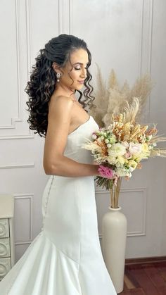 a woman in a white wedding dress holding a large flower bouquet and posing for the camera