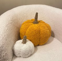 two stuffed pumpkins are sitting on a white chair with a yellow and white pillow