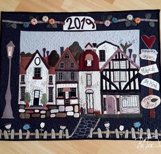 a quilted wall hanging with houses and street signs on the front, along with a sign that says happy new year