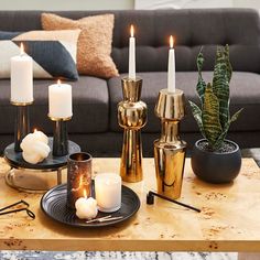 candles are lit on a table in front of a couch and coffee table with other items