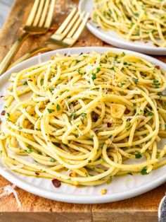 two white plates with spaghetti and parmesan cheese on them next to silverware