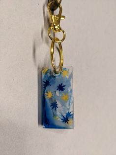 a blue and yellow square shaped object hanging from a gold metal keychain on a white surface