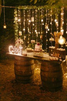 a table topped with cake next to two wooden barrels filled with candles and string lights