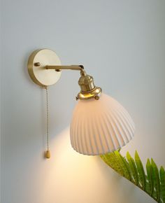 a white wall mounted light with a green plant next to it