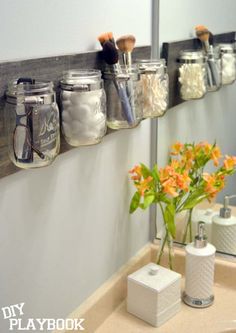 mason jars are hung on the wall above a bathroom sink with flowers in front of it