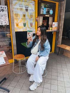 a woman sitting on a stool in front of a coffee shop looking at her cell phone