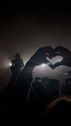 two hands making a heart shape in front of a crowd at a music concert with lights on