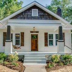 a small white house with brown shutters on the front door and steps leading up to it