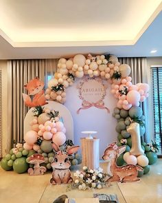 a table topped with lots of balloons next to a wall covered in animals and trees