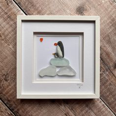 a penguin sitting on top of a rock in a white frame with a red heart