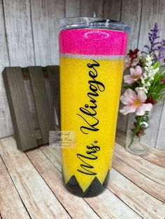 a yellow and pink tumbler sitting on top of a wooden table next to flowers