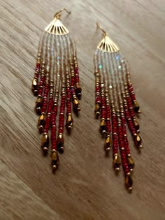 two pairs of red and gold beaded earrings on top of a wooden table next to a pair of scissors