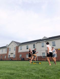 four people are playing frisbee in front of a brick building on the grass