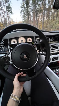 a person driving a car with the steering wheel up and dashboard lights on, in front of some trees