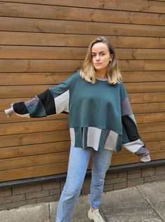 a woman standing in front of a wooden wall wearing jeans and a green sweater with black sleeves