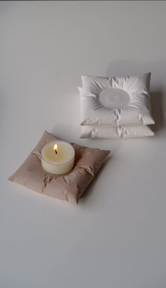 two pillows and a candle on a white surface