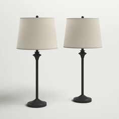 two black lamps with white shades on each lamp are facing opposite directions, one is turned off and the other has a beige linen shade