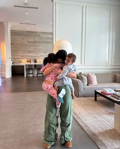 a woman holding two small children in her arms while standing next to a living room