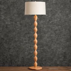 a wooden floor lamp with a white shade on the base and a black wall behind it