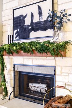 a fireplace decorated for christmas with greenery, candles and a painting on the mantle