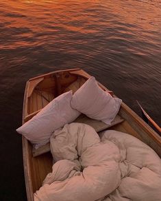 a small boat with pillows and blankets on it in the water at sunset or dawn