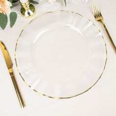 a white table with gold rimmed plates and silverware on it, along with pink flowers