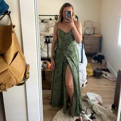 a woman taking a selfie in the mirror wearing a green dress with thigh high slits