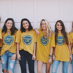 a group of young women standing next to each other wearing matching yellow shirts and jeans