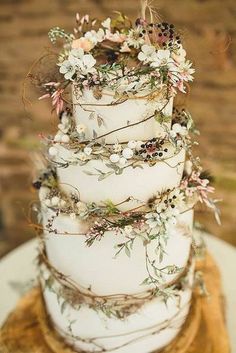 a three tiered wedding cake with flowers and branches on the top is decorated in white frosting