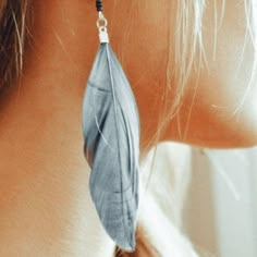 a close up of a woman's ear with a blue feather hanging from it