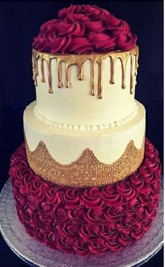 a three tiered cake with red roses and gold icing on it's sides