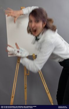 a woman in white shirt and black pants standing next to an easel with her hands on it