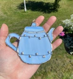 a hand holding a blue teapot shaped brooch