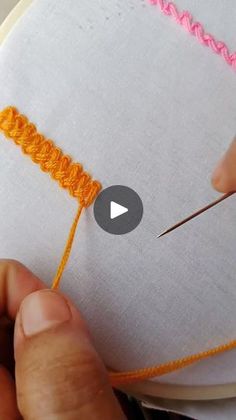 someone is stitching something on a white piece of fabric with orange thread and needle