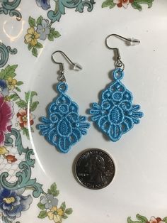 two pairs of blue crocheted earrings sitting on top of a white plate next to a penny