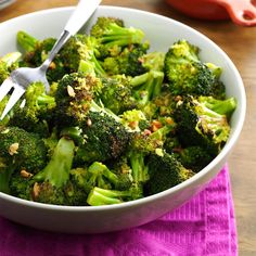 a white bowl filled with broccoli on top of a purple napkin next to a knife and fork