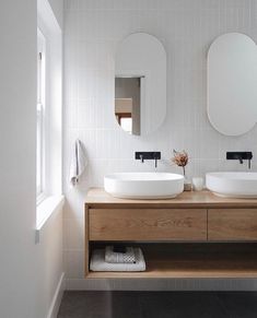 two white sinks sitting on top of a wooden counter in a bathroom next to mirrors