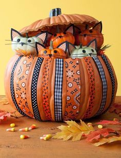 two cats sitting in a pumpkin shaped basket on top of a wooden table with autumn leaves