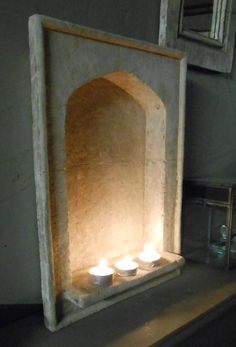 three lit candles are placed in front of a stone arch on a shelf next to a mirror