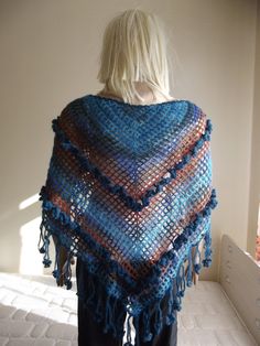 a woman wearing a crocheted shawl with tassels on the sides