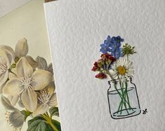 some flowers are sitting in a vase on top of a piece of paper next to another drawing