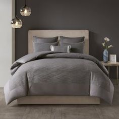 a bed with grey comforter and pillows in a gray room next to two lamps